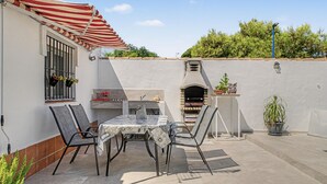 An outdoor patio with a table and chairs, a barbecue grill, and a potted plant.