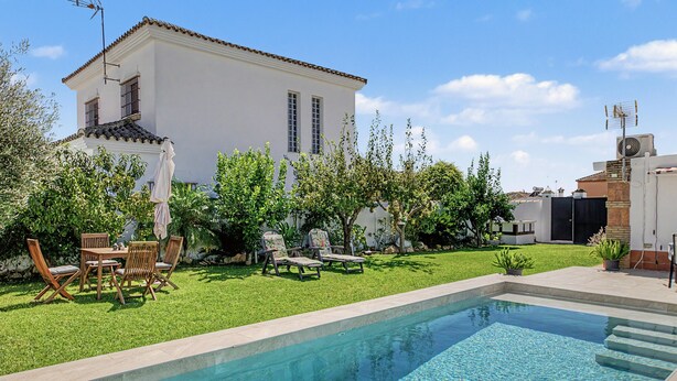 A swimming pool with a clear blue water surface, surrounded by a well-maintained lawn and a patio area with outdoor furniture.