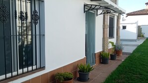 Una casa con fachada de tejas, una ventana con rejas decorativas, una planta en maceta y un pequeño jardín.