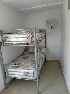 A bunk bed with floral bedding in a small room with tiled flooring and a decorative wall piece.