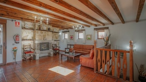 A spacious living room with a fireplace, wooden beams, and a stone wall. - Country House 'Las Eras De Riofrio' with Mountain View, Private Pool and Wi-Fi (Riofrio)