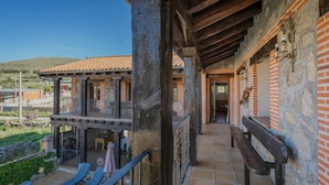 A balcony with a view of a building, a stone wall, and a wooden bench. - Country House 'Las Eras De Riofrio' with Mountain View, Private Pool and Wi-Fi (Riofrio)