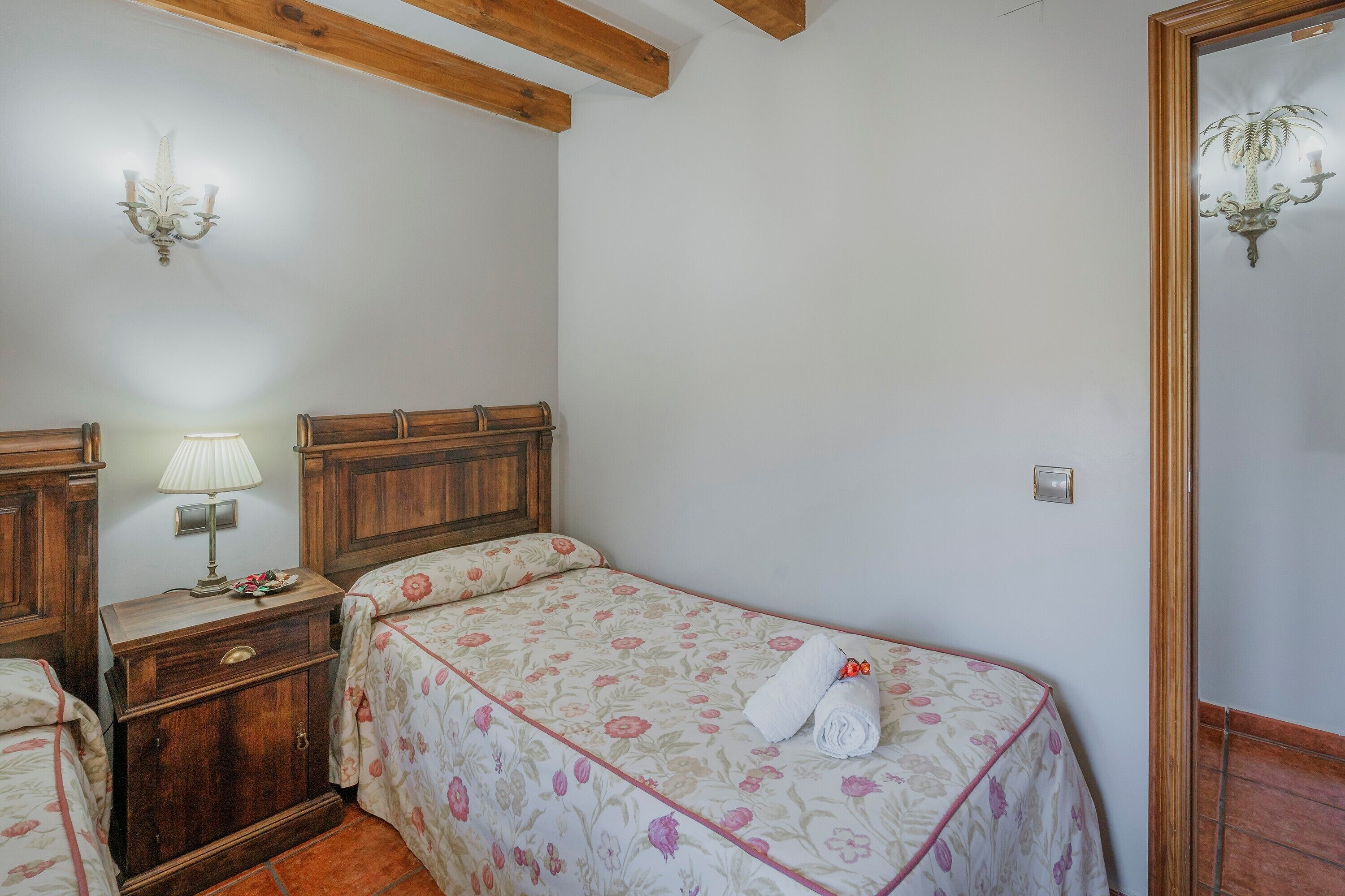 Un dormitorio con una cama individual, cabecera de madera, una mesita de noche con lámpara y un espejo.