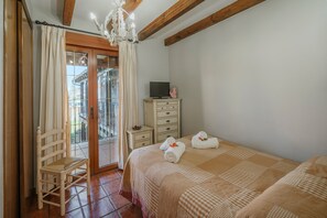 A bedroom with a bed, a chair, a TV on a dresser, and a balcony with curtains.