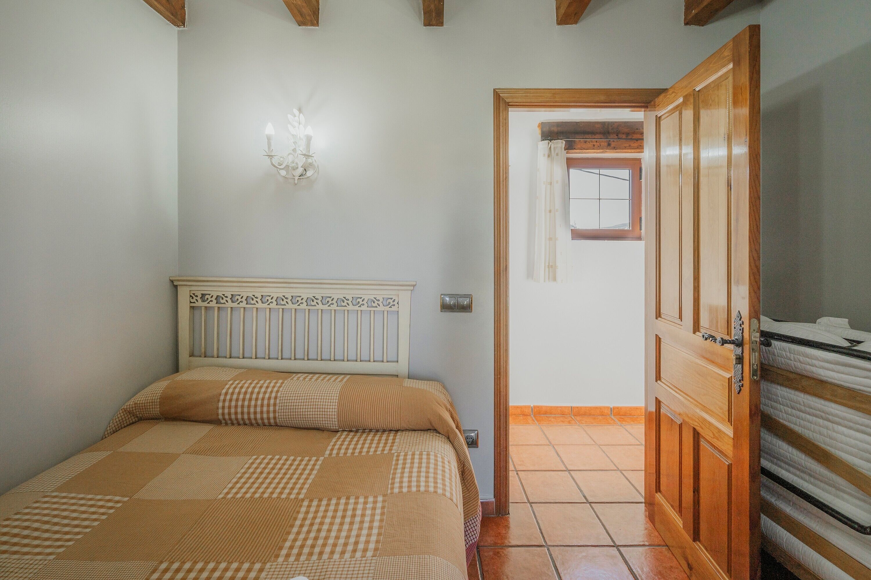 Un dormitorio con cama, lámpara de pared, puerta de madera y suelo de baldosas.