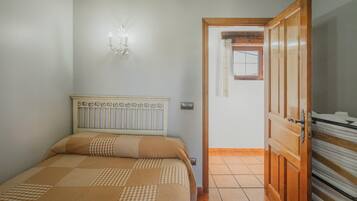 Un dormitorio con cama, lámpara de pared, puerta de madera y suelo de baldosas.