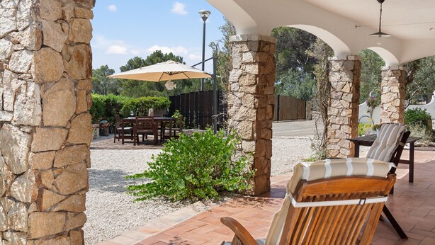 A covered outdoor patio with stone pillars, a table with chairs, and an umbrella.