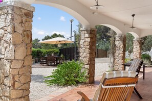A covered outdoor patio with stone pillars, a table with chairs, and an umbrella.