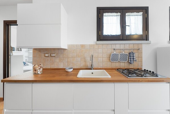 A modern kitchen with a wooden countertop, white cabinets, a sink, a window with curtains, and a gas stove.