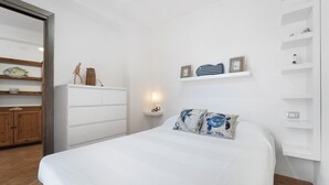 A bedroom with a bed, a wooden wardrobe, a nightstand with a lamp, and shelves with decorative items.