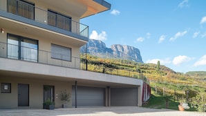Een modern gebouw met een balkon, garage deuren en een bergachtige achtergrond.