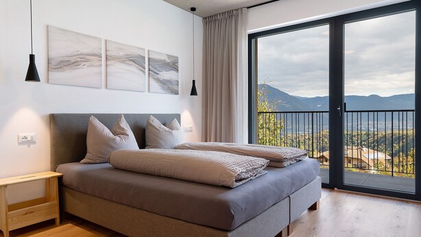 Een slaapkamer met een groot bed, een nachtkastje, een raam met uitzicht op bergen en kunst aan de muur.