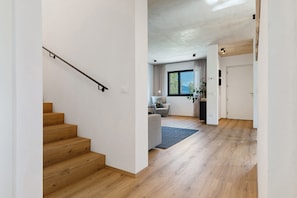 A modern interior with a wooden staircase, a seating area with a sofa and a table, and a view through a window.