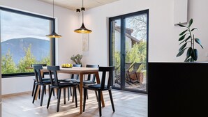 Een eetgedeelte met een tafel en stoelen, grote ramen en uitzicht op bergen.