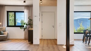Een modern interieur met een houten vloer, een zithoek met stoelen, een bank, een plant en uitzicht op bergen door een raam.