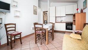 A compact kitchen with white cabinets, a dining table with chairs, a sofa, and a TV mounted on the wall.