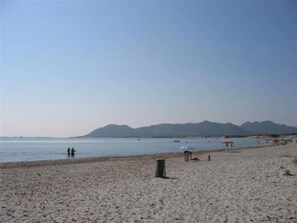 Ein Strand mit blauem Himmel, ruhigem Meer und fernen Bergen.