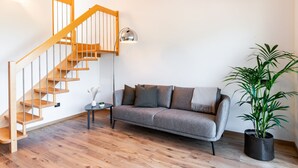 En stue med en trætrappe, en grå sofa, et lille sofabord, en gulvlampe og en potteplante.