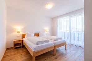 A bedroom with two beds, bedside lamps, a wooden nightstand, and a large window with sheer curtains.