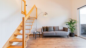 A modern living room with a wooden staircase, a grey sofa, a small side table, a floor lamp, and a potted plant. - Apartment 'Preiss Type B' with Mountain View, Balcony and Wi-Fi (Schenna)