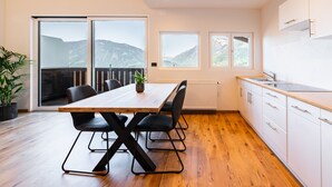 A modern kitchen with a wooden table and chairs, a view of mountains through large windows, and a balcony. - Apartment 'Preiss Type B' with Mountain View, Balcony and Wi-Fi (Schenna)