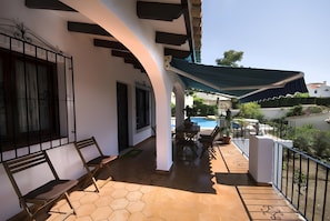 Een overdekt terras met een zwembad op de achtergrond.