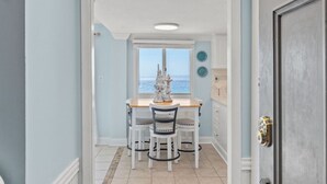 A hallway leading to a dining area with a view of the ocean, a white table, and four chairs. - Paradise Found On the Beach PH16 (Panama City Beach)