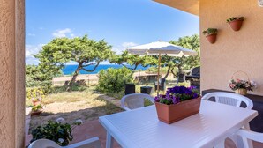 A patio with a white table, chairs, potted plants, and a view of the sea.