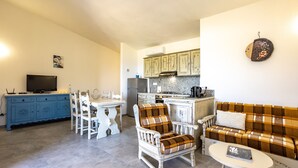 A living room with a sofa, armchair, and coffee table, a dining area with a table and chairs, and a kitchen with cabinets and appliances.