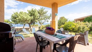 Un patio exterior con una mesa, sillas, una parrilla y vistas al mar.