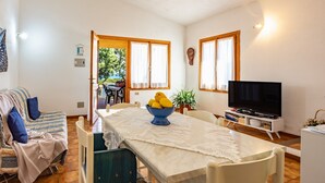 Una sala de estar con un sofá, una mesa de comedor con un frutero, un televisor y vistas al exterior.