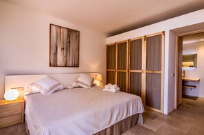 Une chambre à coucher comprenant un lit, des lampes de chevet, une tête de lit en bois, une grande œuvre d’art et une armoire aux portes coulissantes.