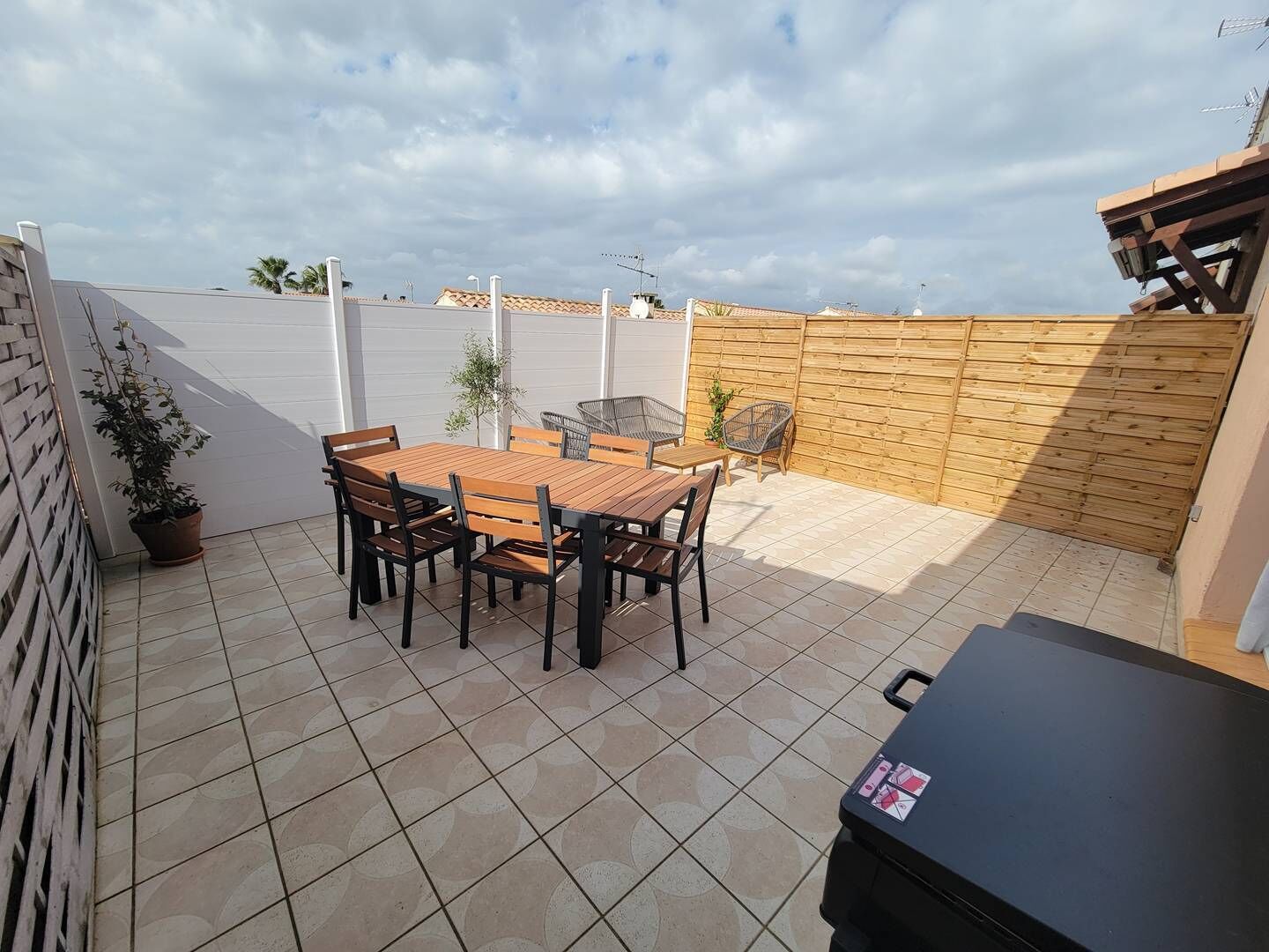 Eine Terrasse mit Holztisch und -stühlen, einem Grill und einem Blumentopf.