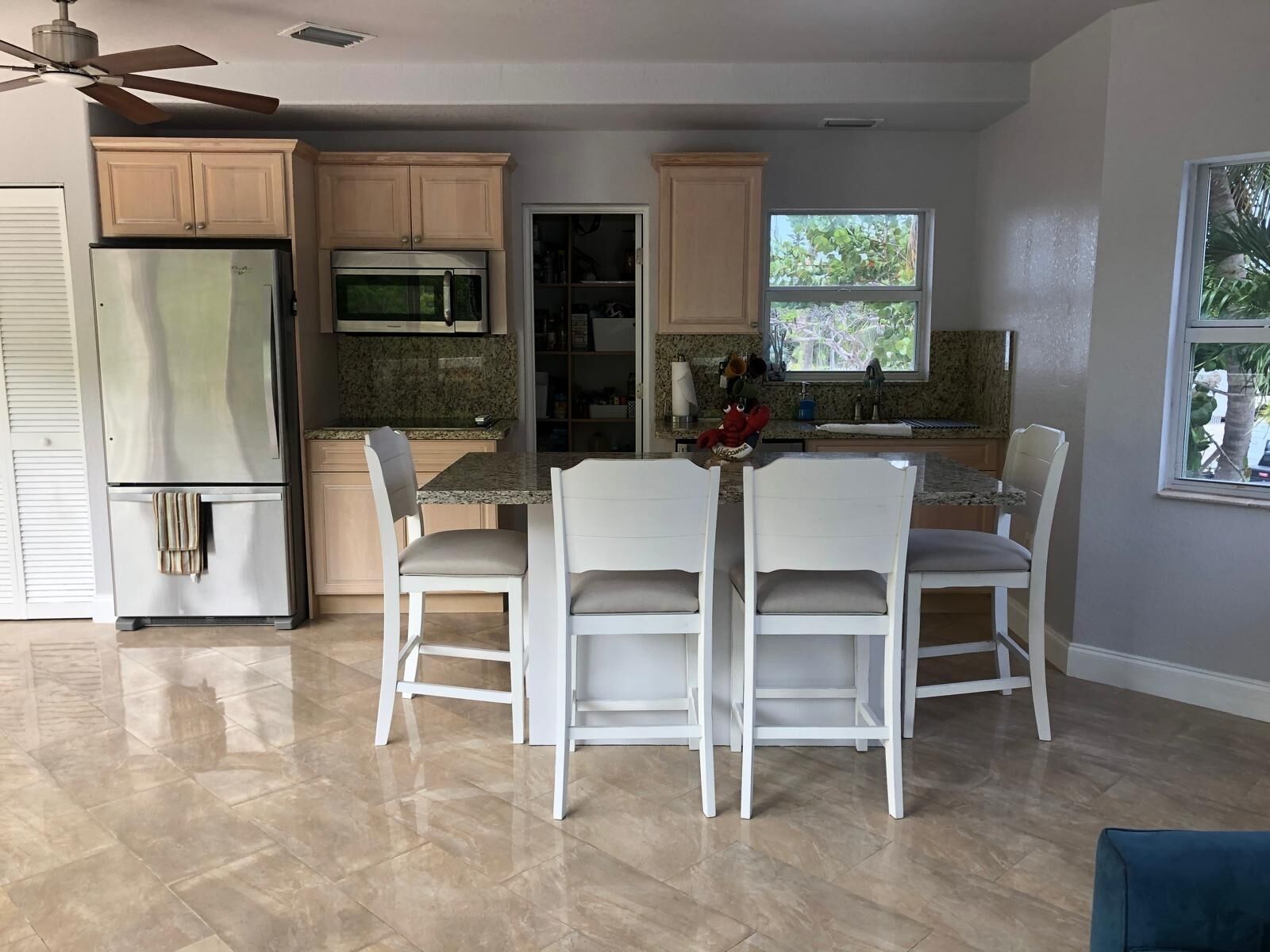 A modern kitchen with a double-door refrigerator, a built-in oven, and a microwave. There is a dining area with a white table and chairs, and a window providing natural light.