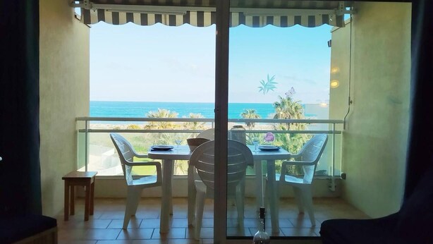 A balcony with a table and chairs, overlooking a beach and palm trees. - Splendid sea view for this T2 in residence with swimming pool - 4GOEL248 (SAINT CYPRIEN PLAGE)