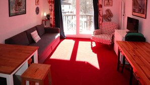 Een woonkamer met een rood tapijt, een bank, een gestipelde fauteuil, een houten tafel en een televisie.