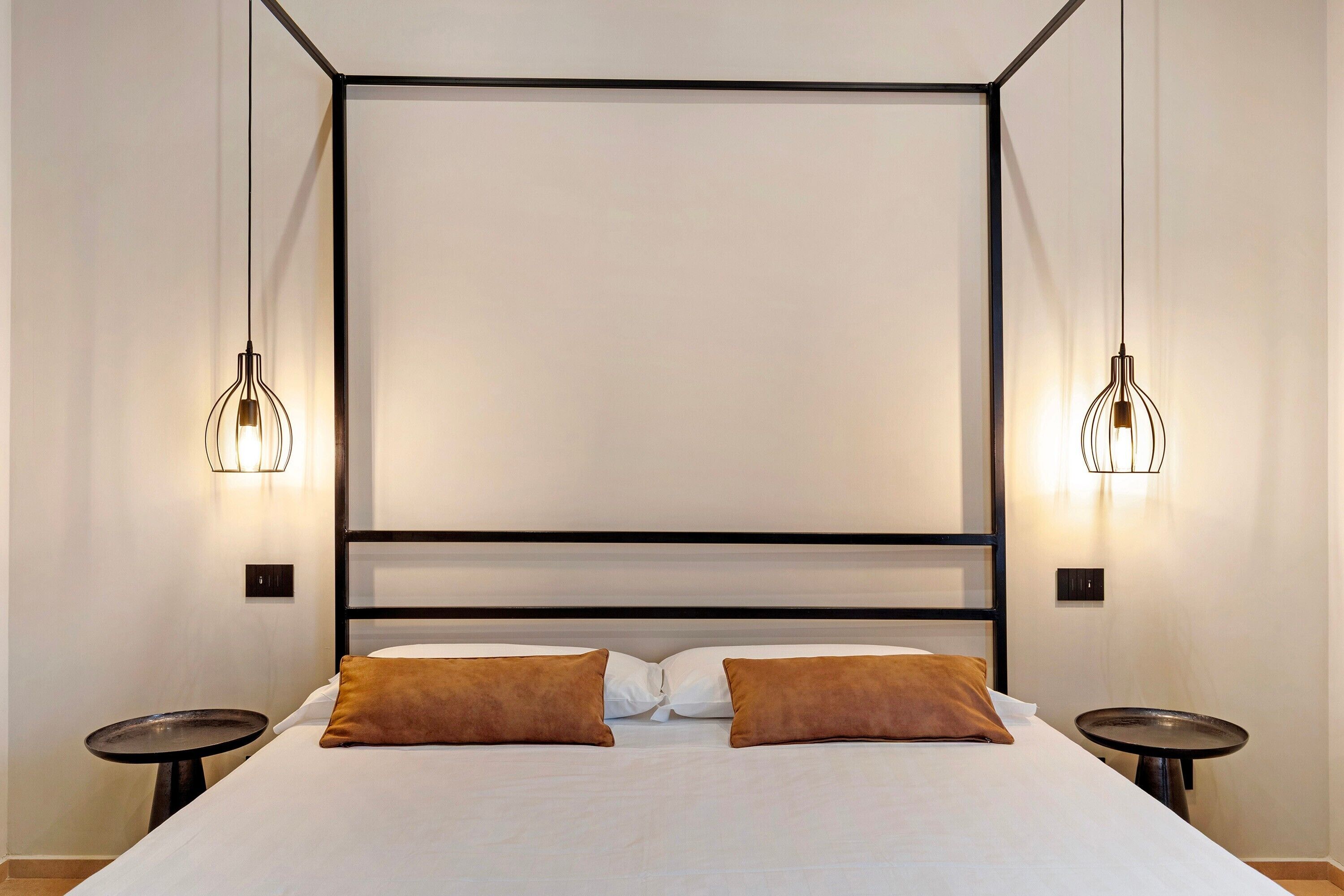 Uma cama com estrutura de metal preta, duas mesas de cabeceira e duas luminárias fixadas na parede.