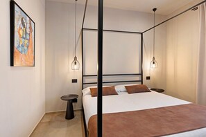 A modern bedroom with a four-poster bed, pendant lighting, a small round table, and a painting on the wall.