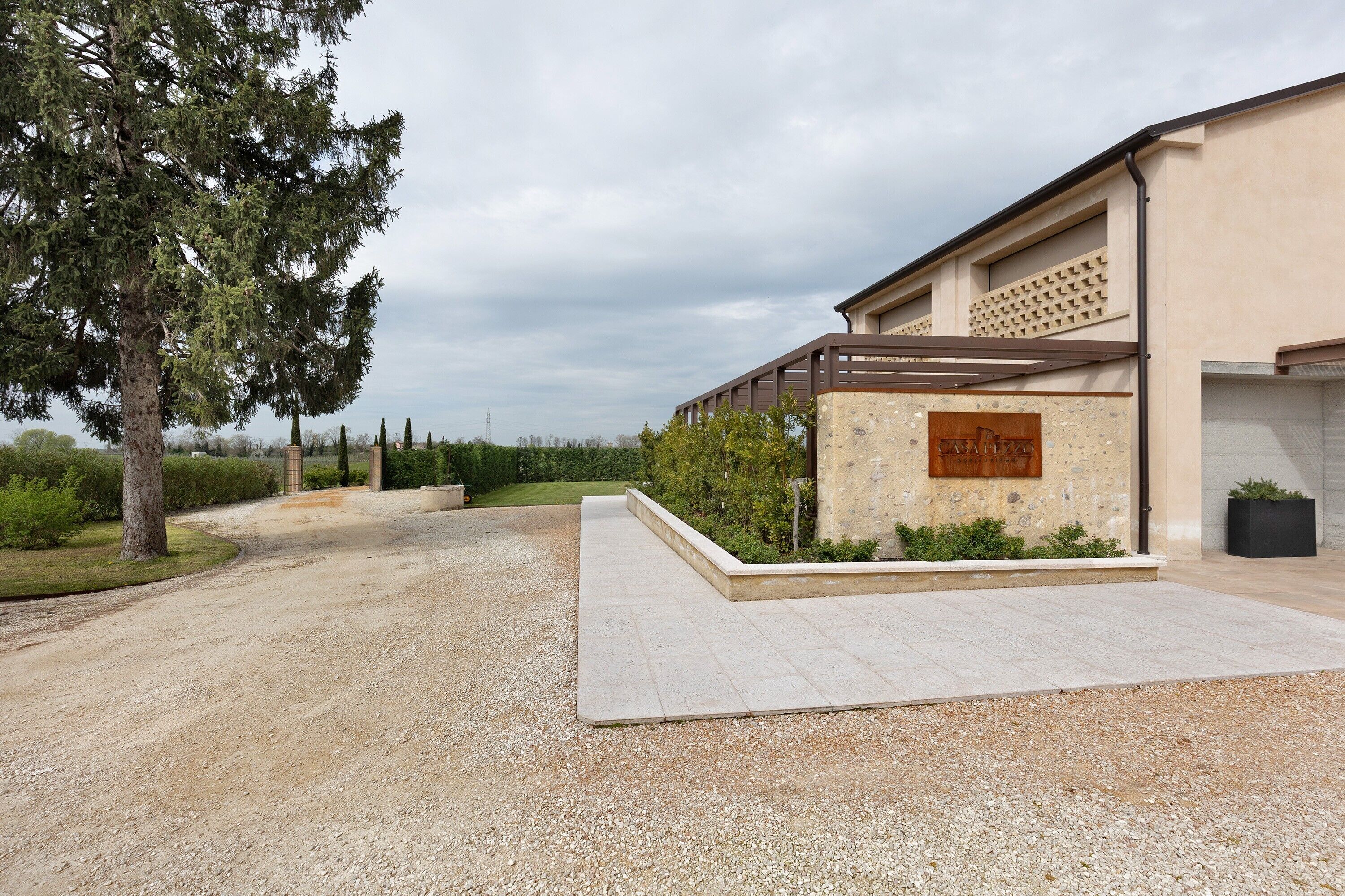 Een gebouw met een grindpad, een pergola en een stenen muur met een plaquette.