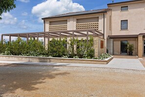Un bâtiment moderne doté d’un espace extérieur couvert, d’une allée en gravier et d’un jardin agrémenté de fleurs blanches.