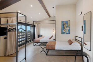 A modern hotel room with a large window, a bed, a seating area, and a wardrobe with hanging clothes.