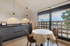 A modern kitchen with a dining area, large windows, and a view of greenery.