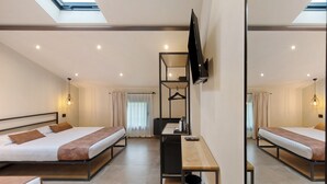 Habitación de hotel con dos camas, un escritorio, un televisor y un tragaluz.