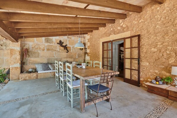 A rustic dining area with a wooden table and chairs, a stone wall, and a wooden ceiling. - Finca 'Son Garreta' with Views of the Tramuntana, Private Pool and Wi-Fi (El Palmer)