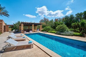 A rectangular swimming pool with clear blue water, surrounded by lounge chairs and a pergola.