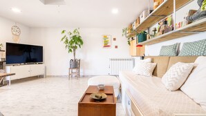 Een woonkamer met een televisie, bank, salontafel en planken met diverse spullen.