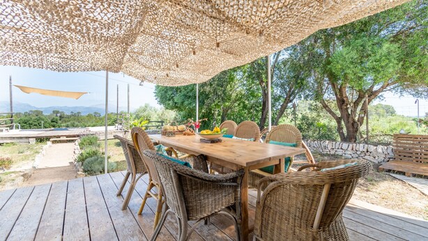Een eethoek buiten met rieten stoelen en een houten tafel, omringd door een geweven luifel.