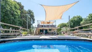 Een zwembad met een houten terras, een beschaduwd zitgedeelte en een gebouw met een balkon.