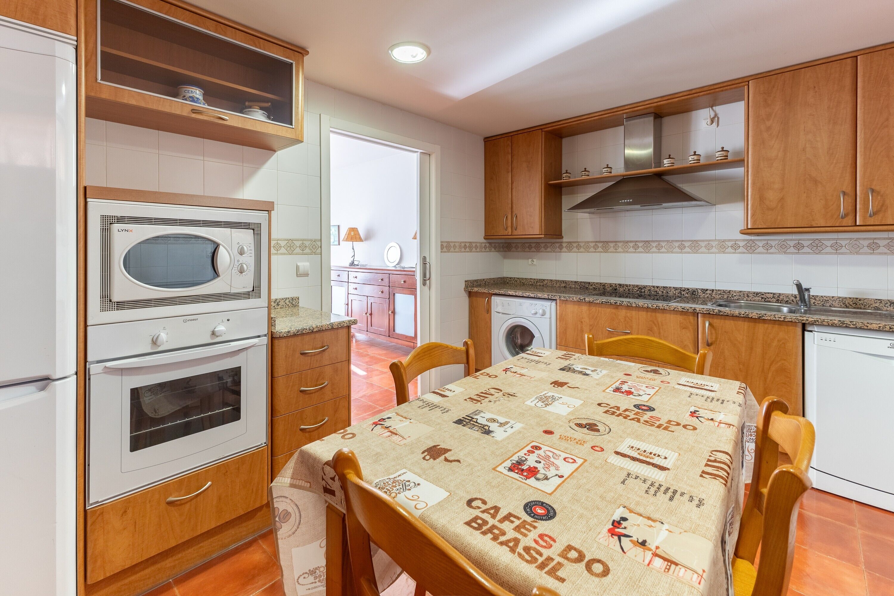 Una cocina con armarios de madera, microondas, horno y una mesa con mantel.
