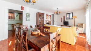Un comedor con una mesa y sillas de madera, una cocina al fondo y una sala de estar con sofá y televisor.